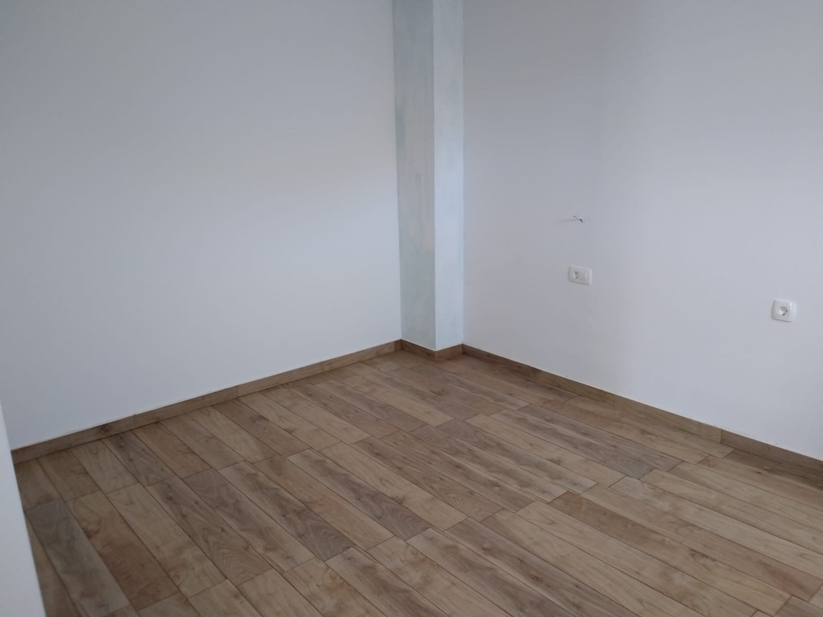 Uređena prazna soba s bijelim zidovima i keramičkim podom u izgledu drva