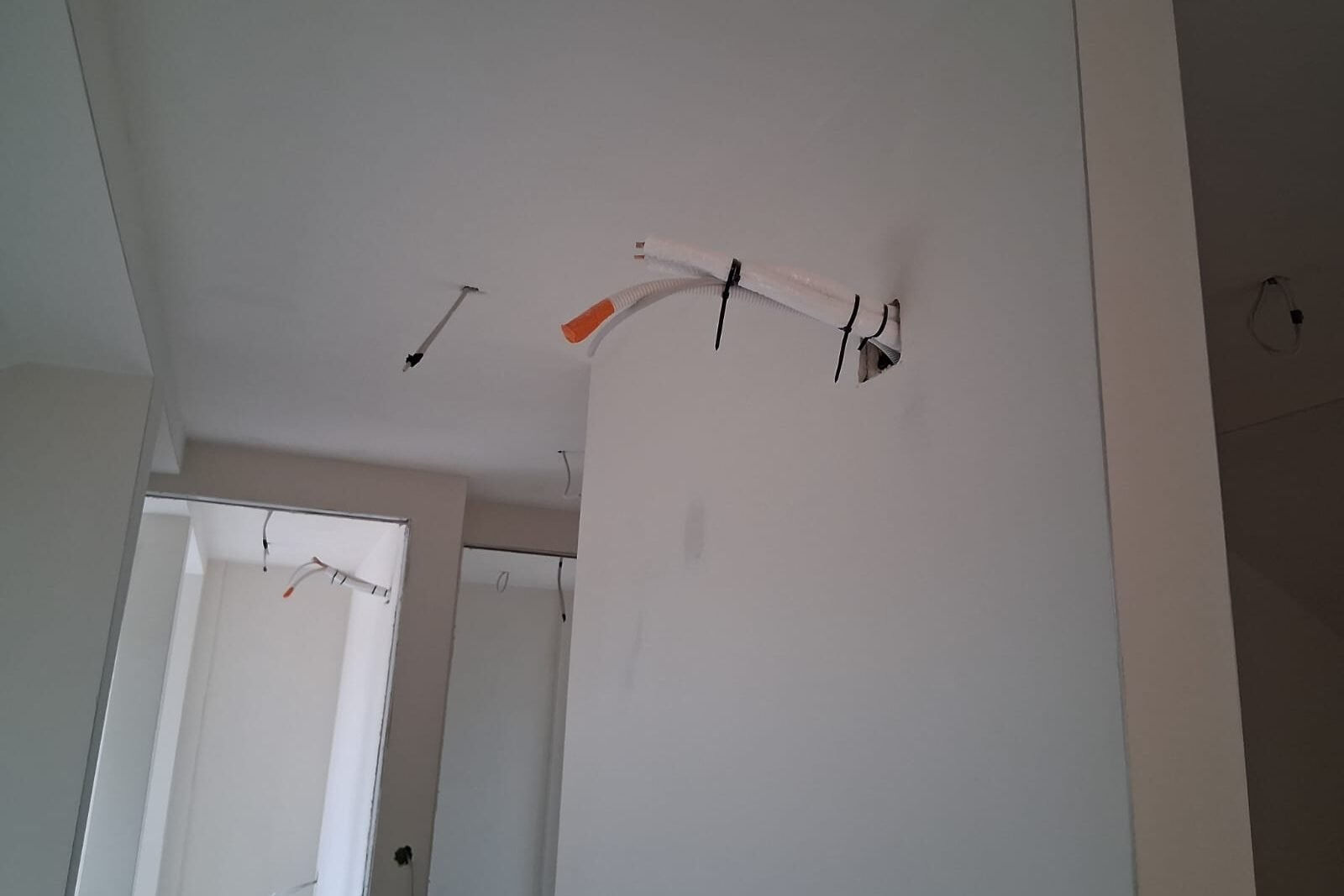 Provedene cijevi i električni vodovi za zidnu klimatizacijsku jedinicu u bijeloj prostoriji