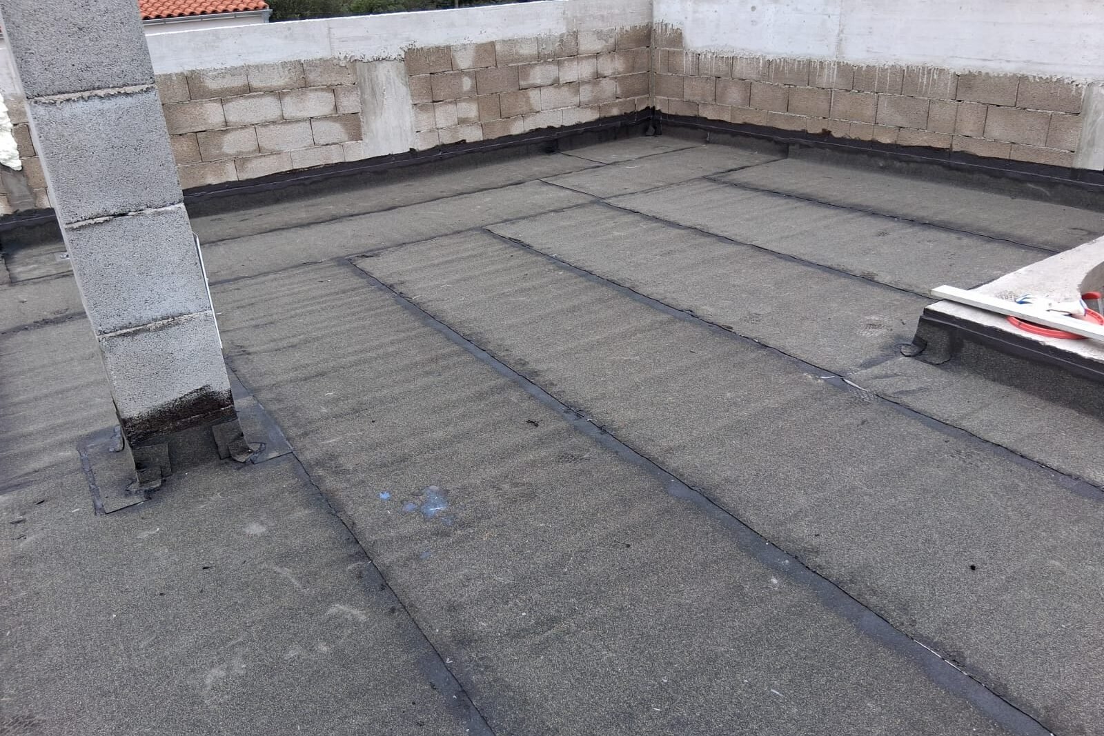 Šira ploha ravnog krova prekrivena bitumenskom membranom uz zidani parapet i dimnjački stup